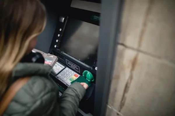 junge Frau steckt Karte in Bankomaten