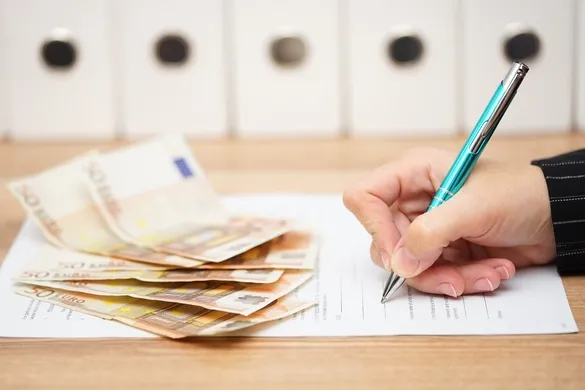 Person unterzeichnet Vertrag auf dem Bargeld liegt