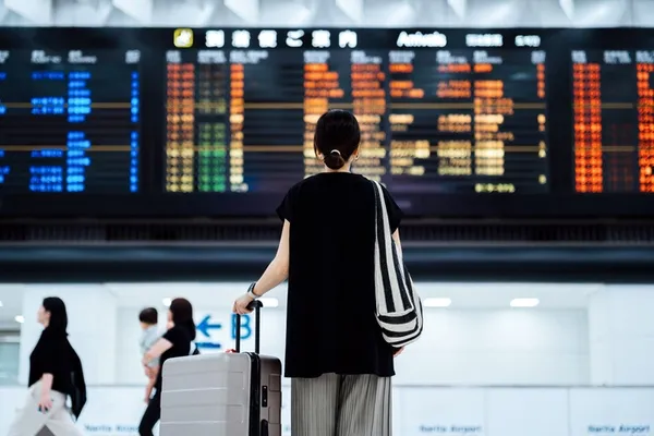 Reisende mit Koffer vor einer Abflugtafel am Flughafen