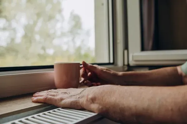 Hand auf einer Heizung vor Fenster
